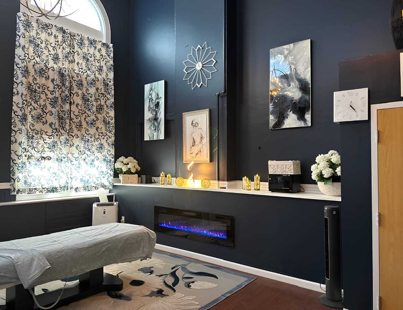 Massage room with decorative art, flowers, and an electric fireplace under ambient lighting.