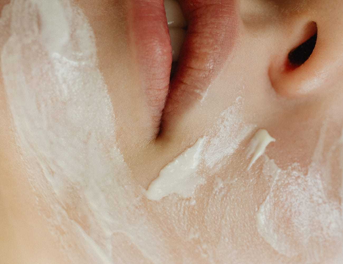 Close-up of a person's face with white cream applied around the lips and cheek.