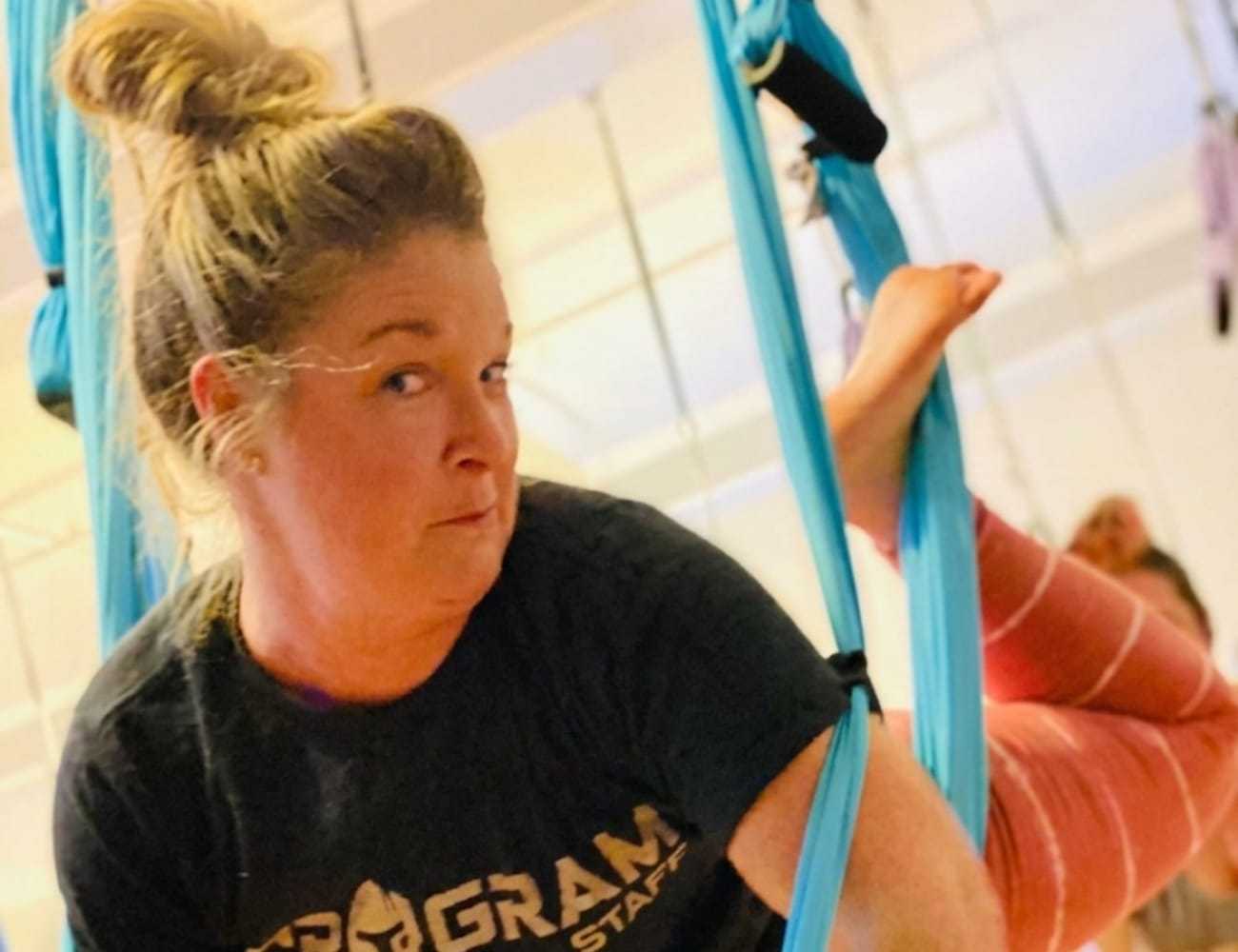 A woman practicing aerial yoga on blue silks indoors.